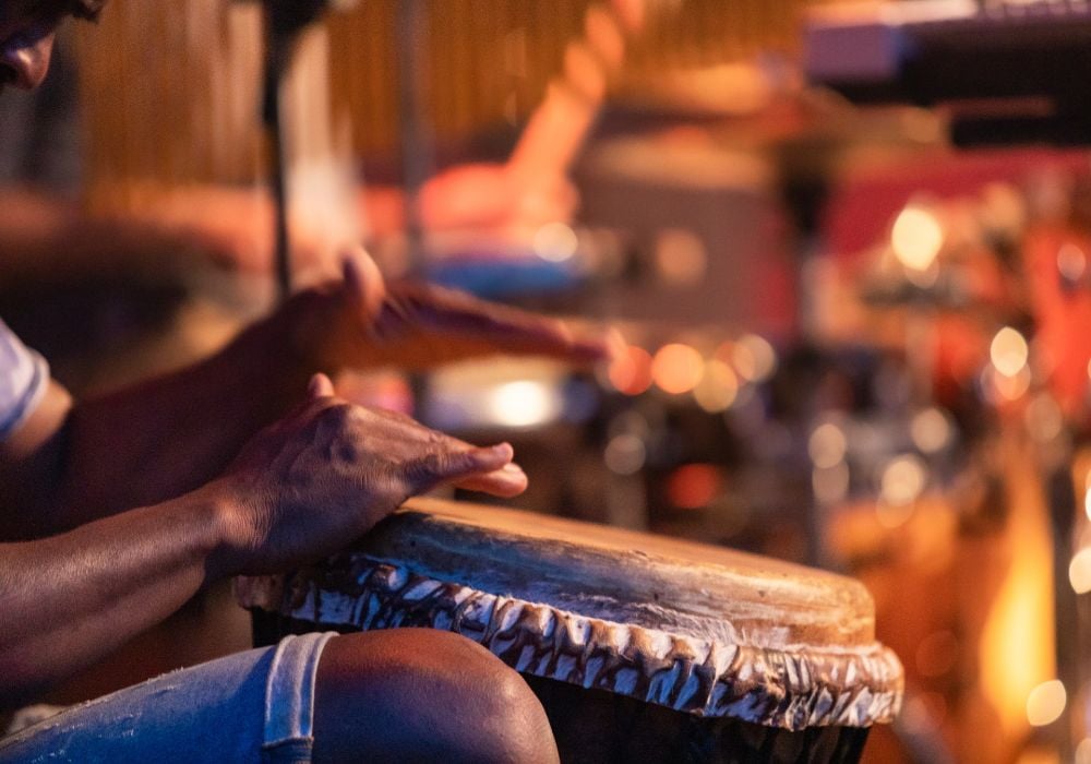 Close-up of a man's hands playing on an African djembe drum; selective focus on hands with blurry background.
