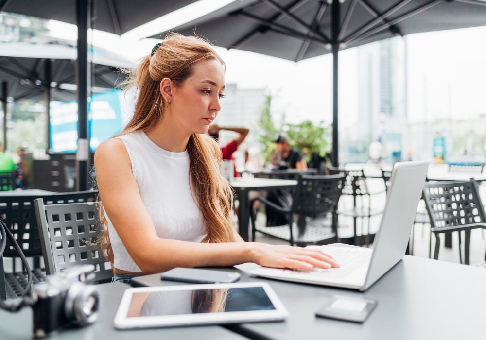 Young woman working remotely sitting on a bar using laptop