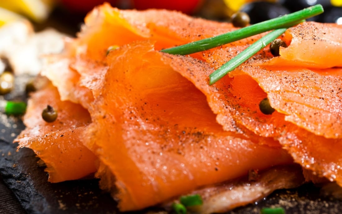 A close-up view of a slate tray with smoked salmon on a rustic wood table.